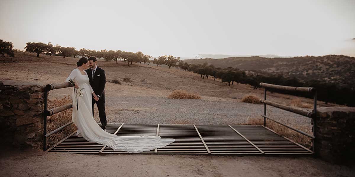 Una pareja de novios posando el día de su boda con una dehesa de fondo.