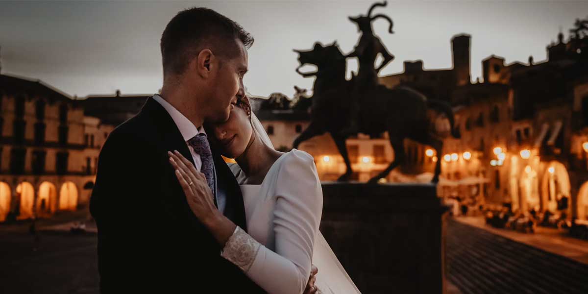 Pareja de recién casados abrazados en la Plaza Mayor de Trujillo al atardecer.